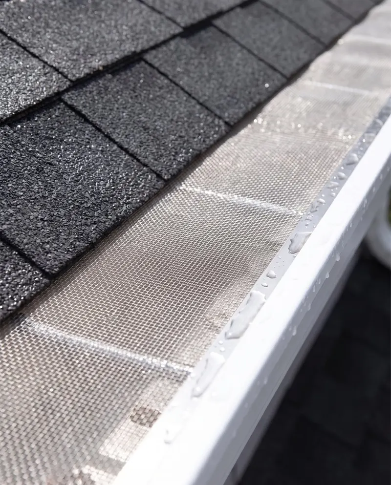 Micro-mesh gutter guard tucked under charcoal shingles, beaded with rainwater